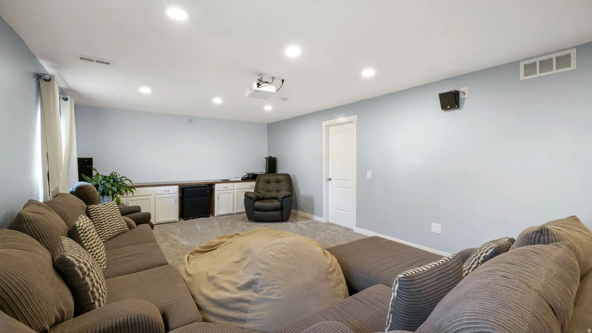 Spacious entertainment area featuring recessed lighting, a built-in projector, and wall-mounted speakers