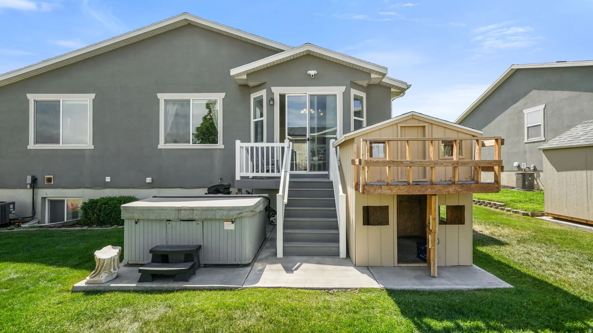 Rear exterior featuring a sliding glass door, white deck railing, and a private hot tub on a concrete patio
