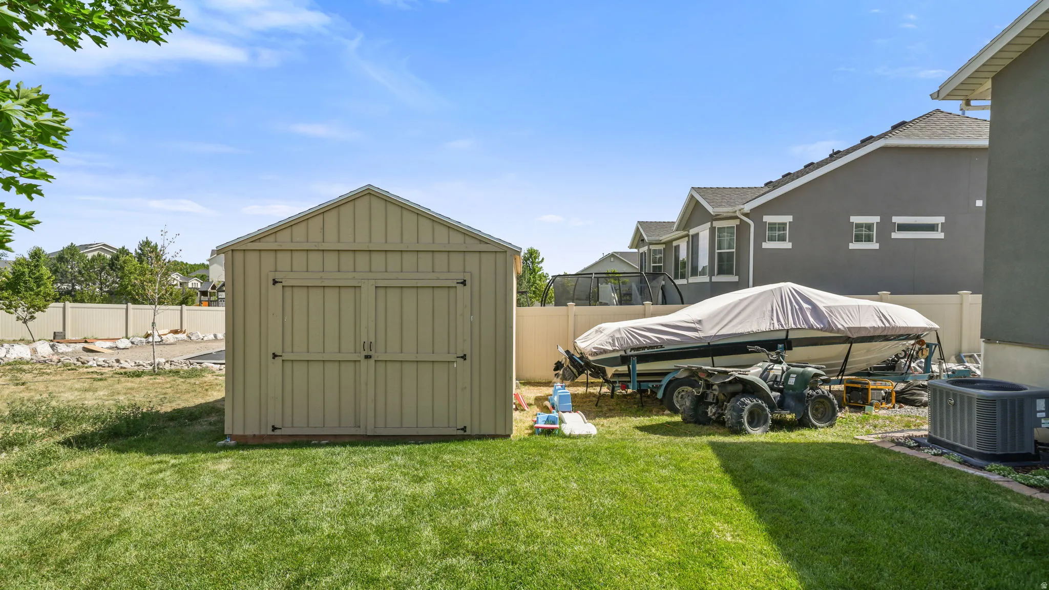 Expansive backyard featuring a manicured lawn, a detached storage shed with double doors, and a partial rock garden with mature trees