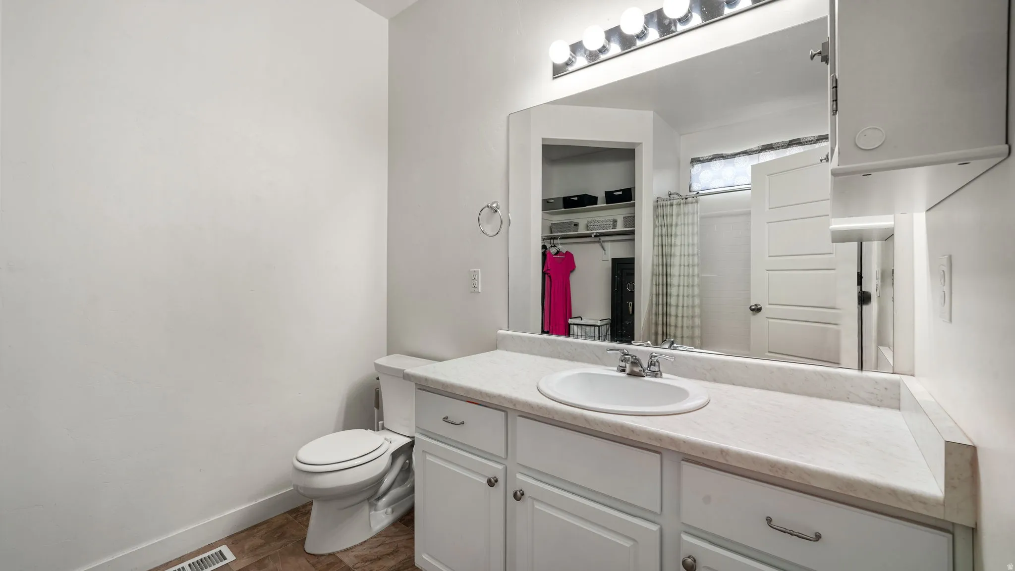 Bathroom featuring a single vanity with a white countertop and integrated sink, a large wall-mounted mirror, overhead vanity lighting, and white cabinetry