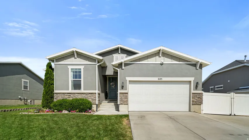 Contemporary grey stucco exterior featuring a stone accent foundation, a white two-car garage, and a manicured front lawn