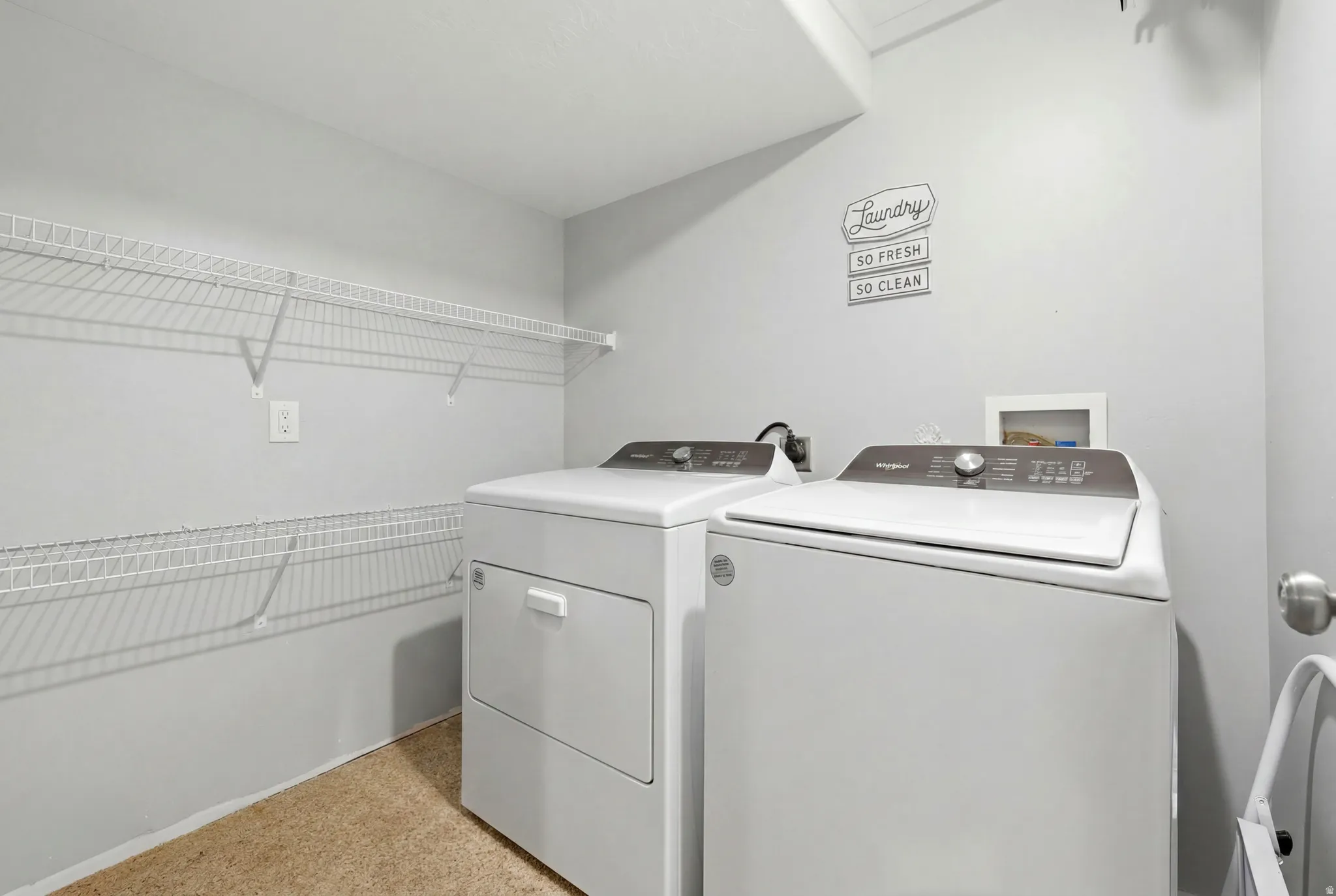 Dedicated laundry area featuring wire shelving, light grey wall paint, and beige textured flooring