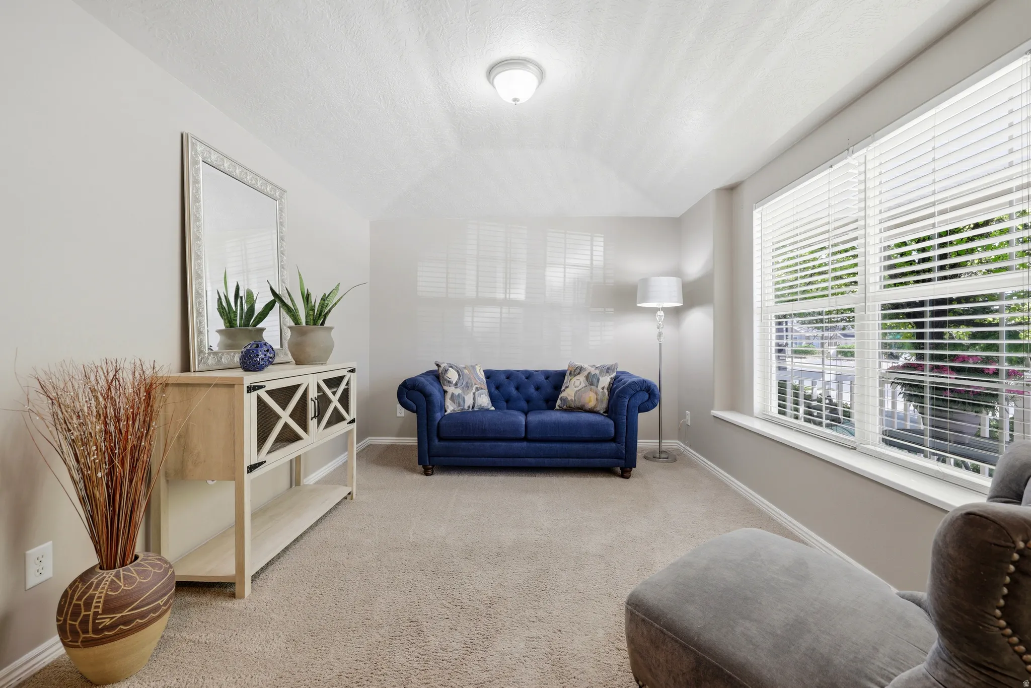 Vaulted ceiling room featuring light-toned carpeting, neutral wall paint, and multiple windows with horizontal blinds