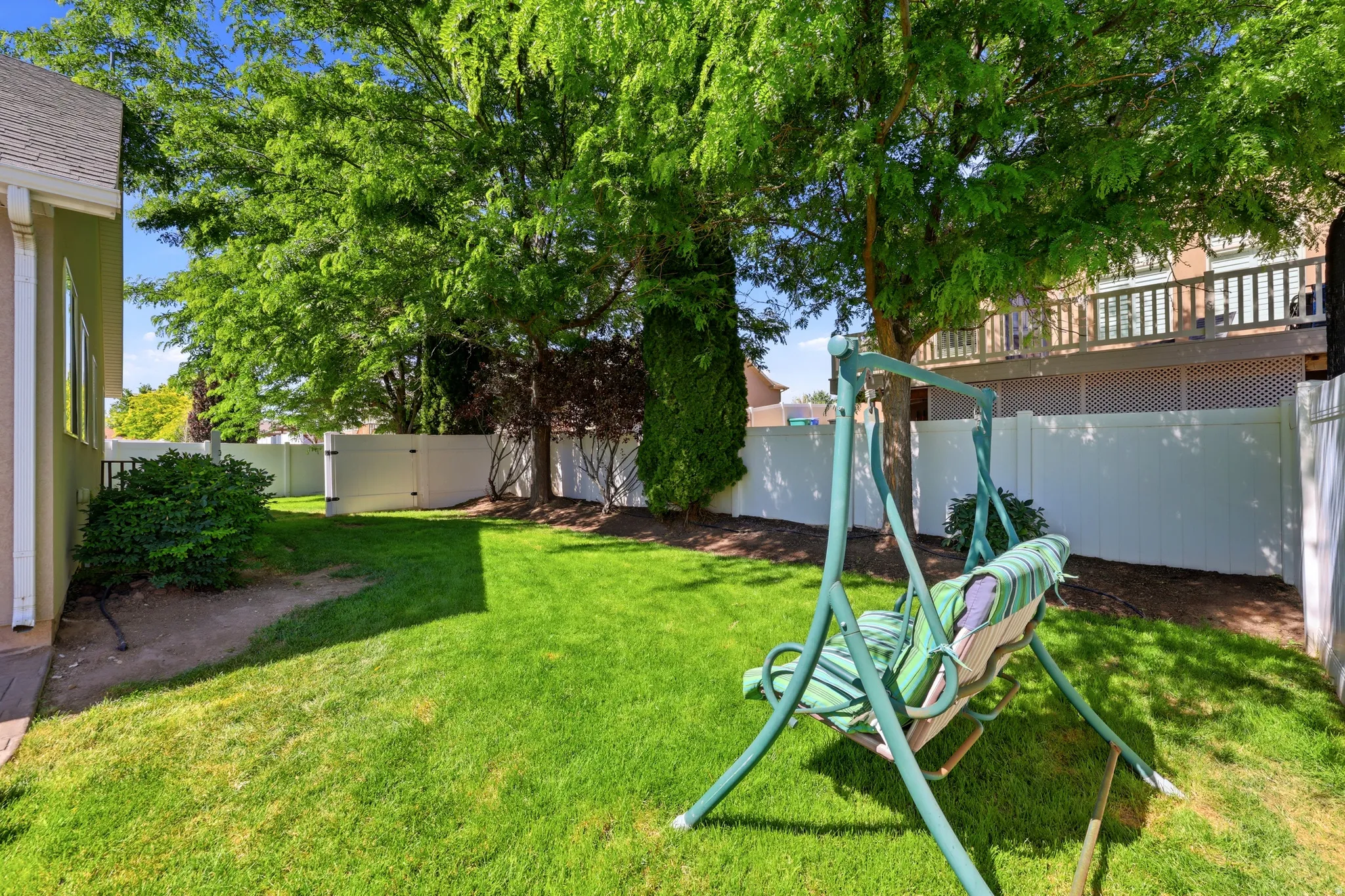 Spacious outdoor area featuring a lush green lawn, mature shade trees, and a privacy fence