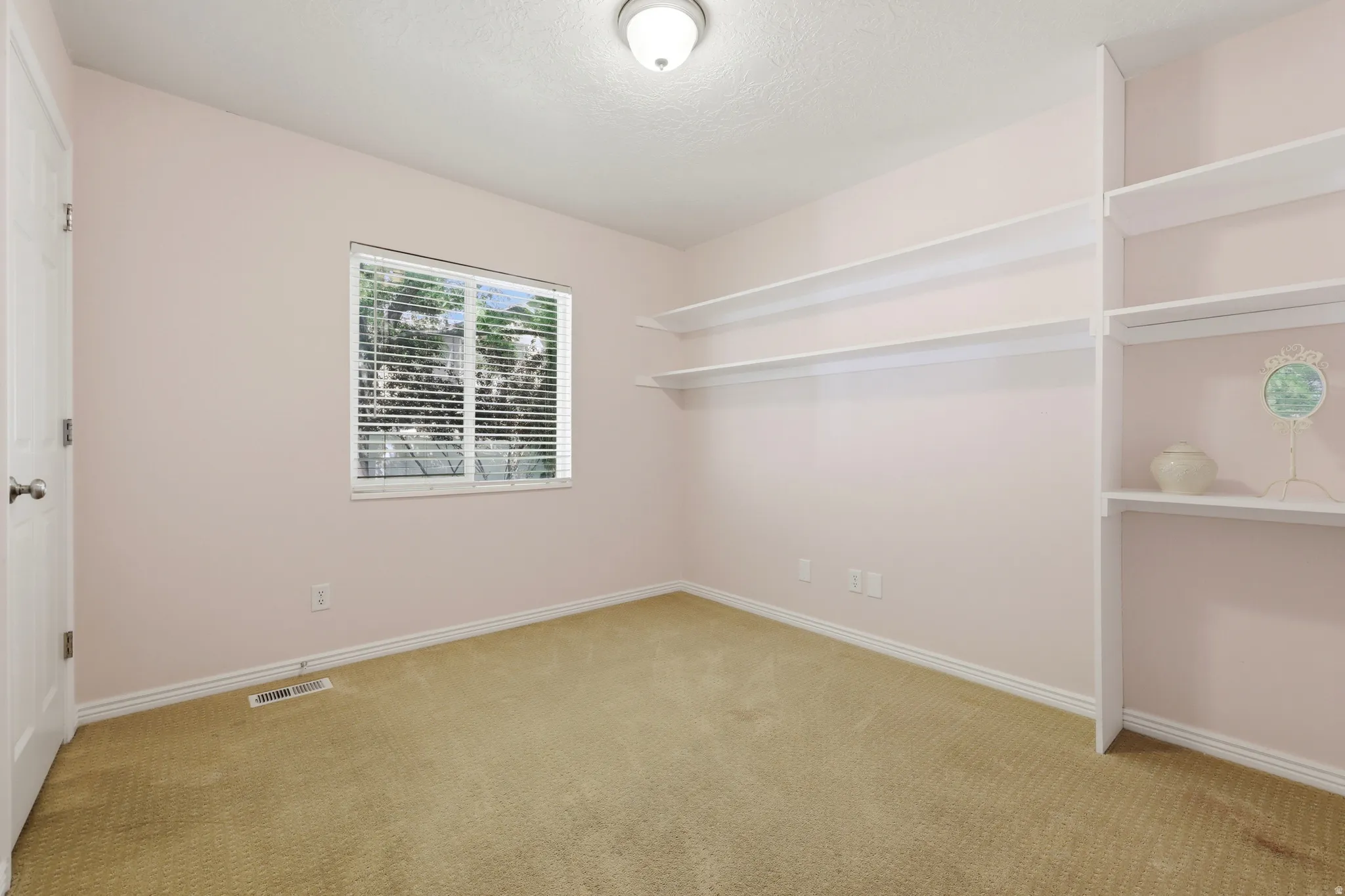 Carpeted room featuring a window with horizontal blinds, built-in shelving, white baseboards, and a flush mount ceiling light fixture