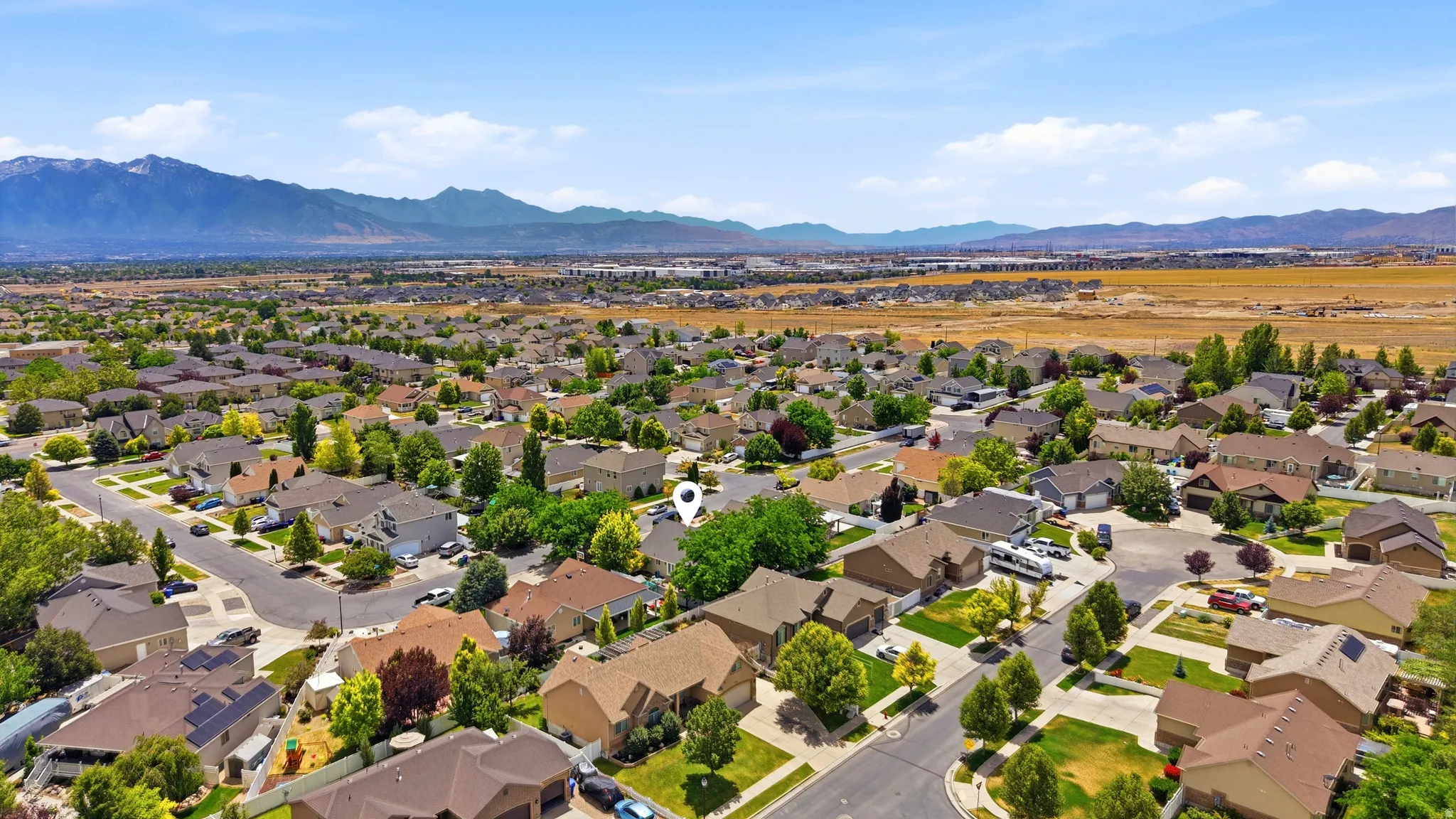 Suburban residential area with established homes and mature trees, set against a backdrop of distant mountains and open land