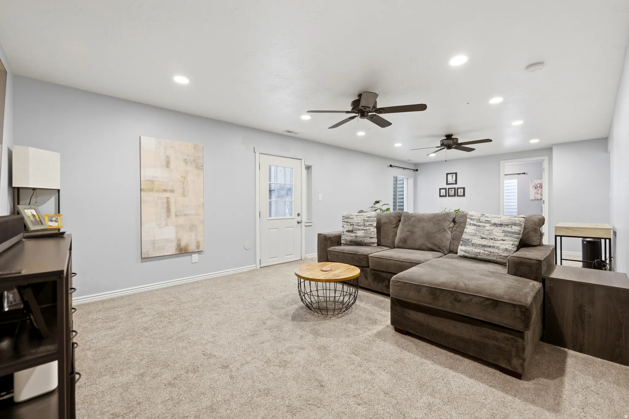 Expansive carpeted room featuring light gray walls, multiple recessed lights, two ceiling fans, and a white door with glass paneling
