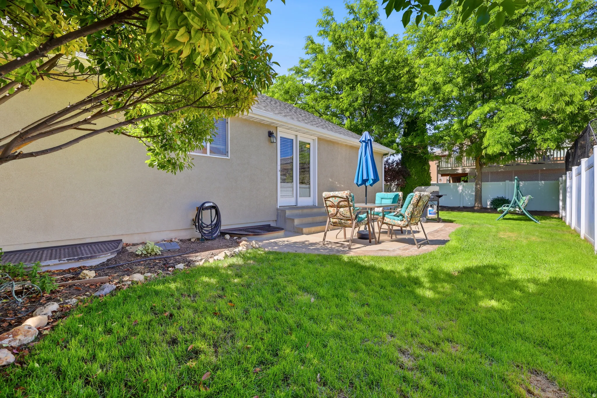 Expansive backyard featuring a manicured lawn, a paved patio area, and mature trees providing natural shade