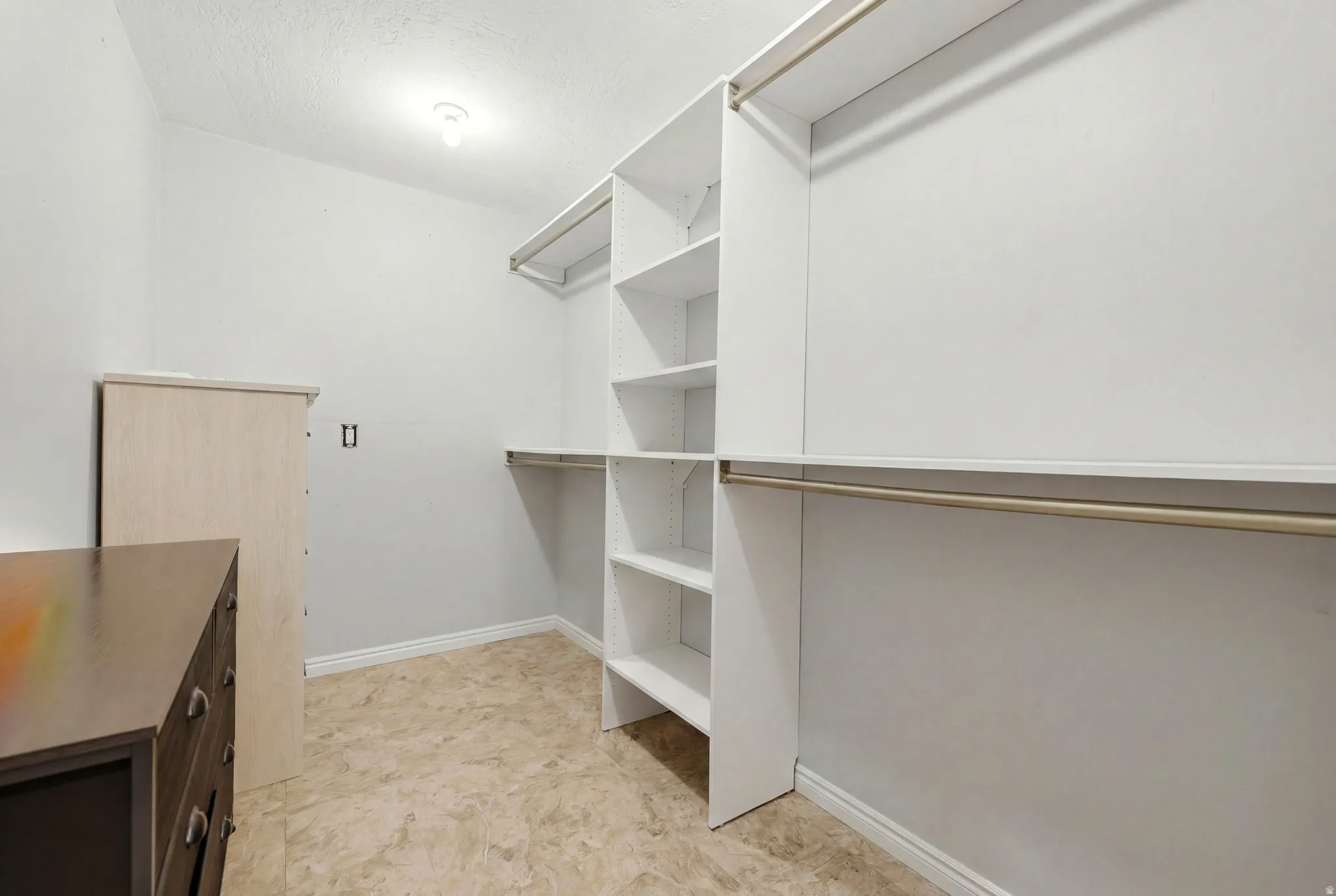 Spacious closet featuring white built-in shelving, hanging rods, and light-colored flooring