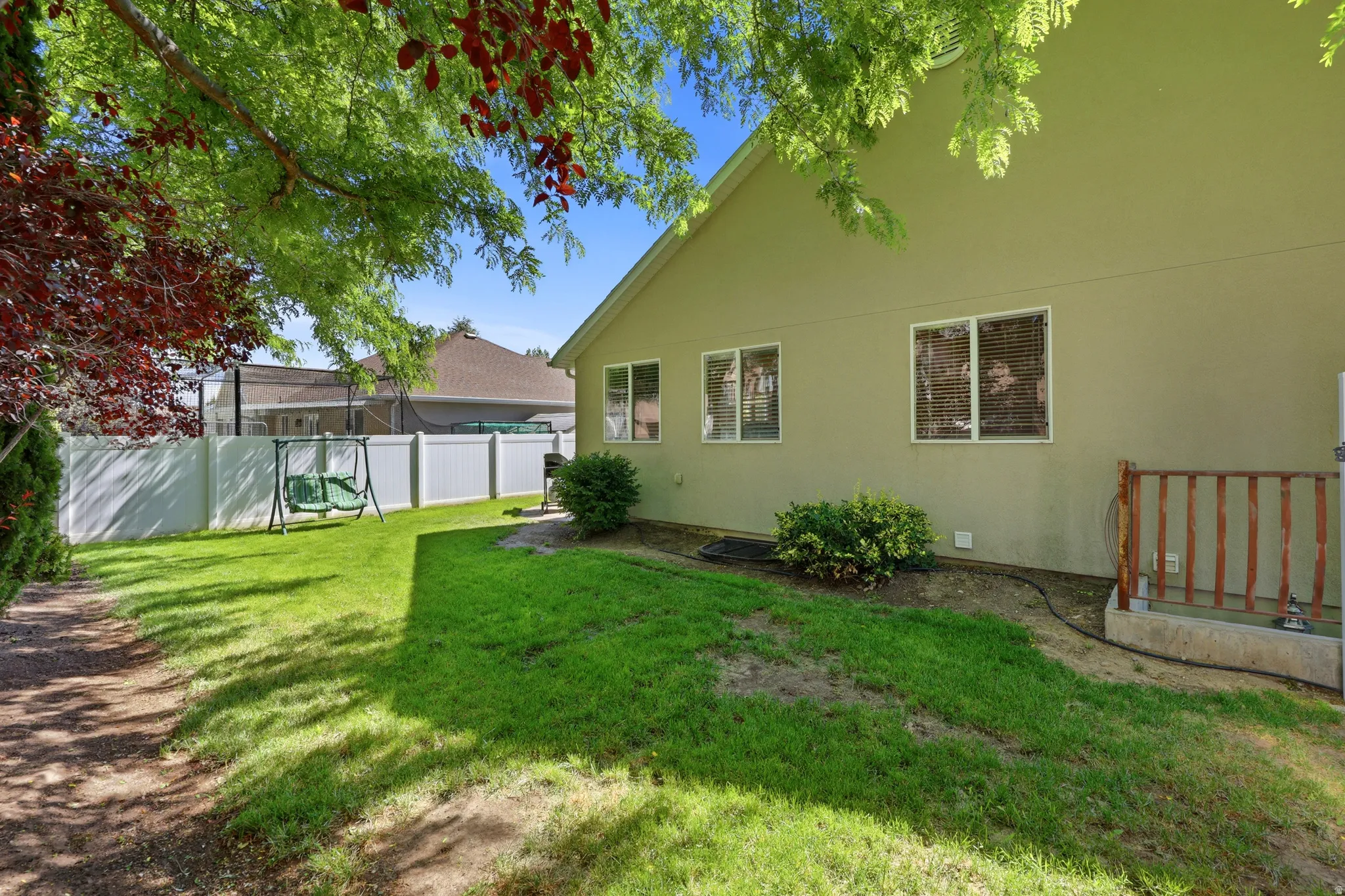 Spacious rear yard with a manicured lawn, full privacy fencing, mature trees, and a ground-level patio with wood railing