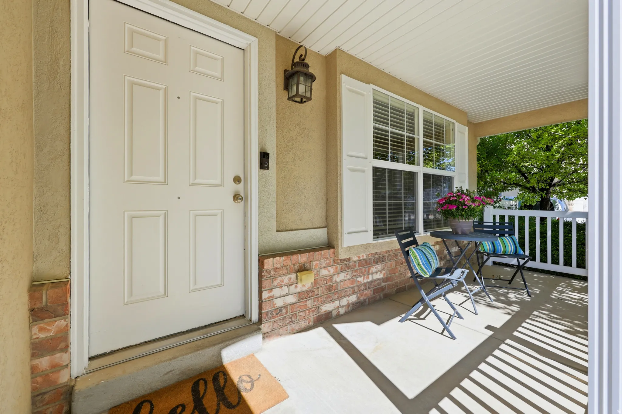 Covered front porch featuring a paneled entry door, brick accents, and a window with louvered shutters