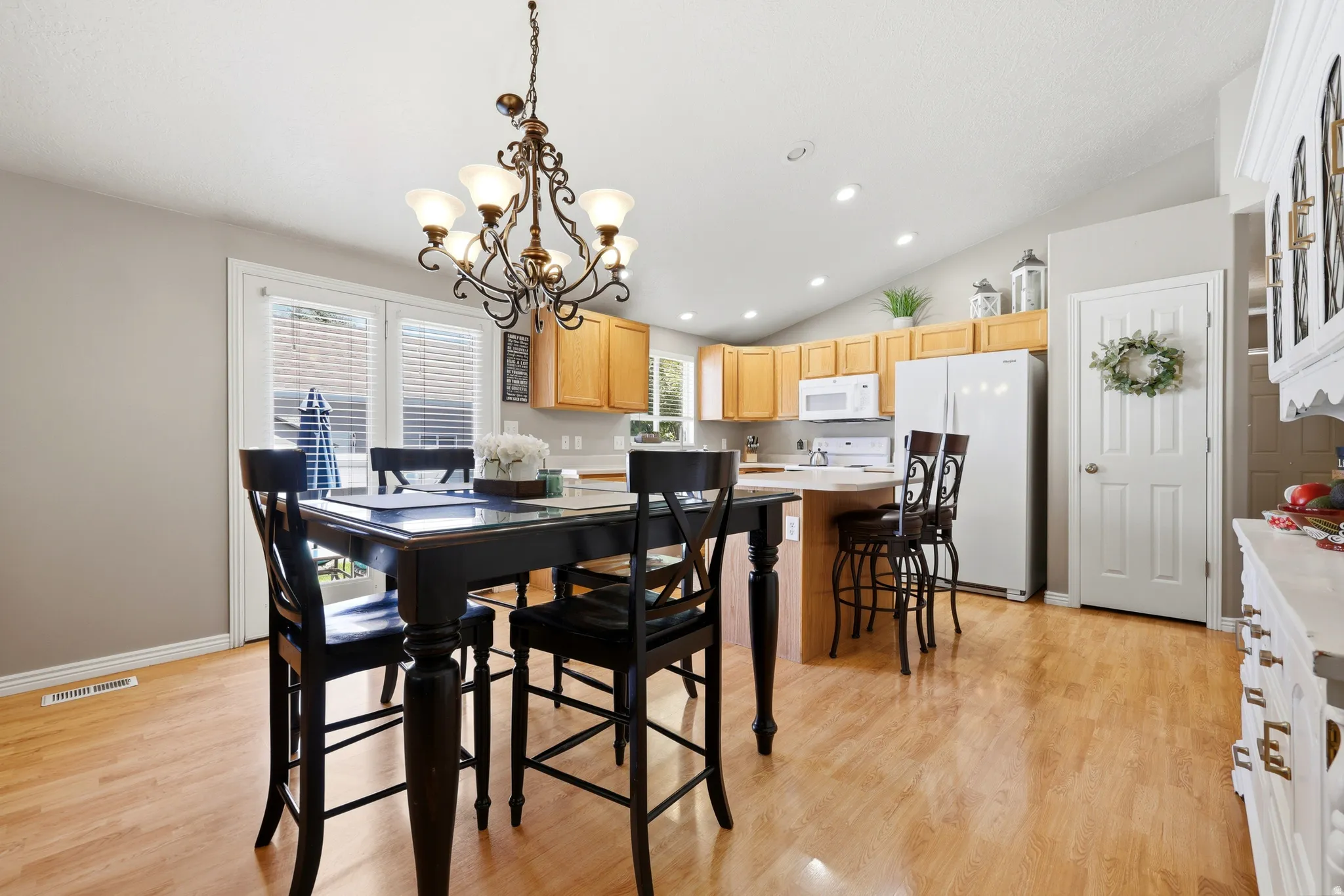 Open-concept dining and kitchen area featuring wood-finish flooring, a vaulted ceiling, and recessed lighting