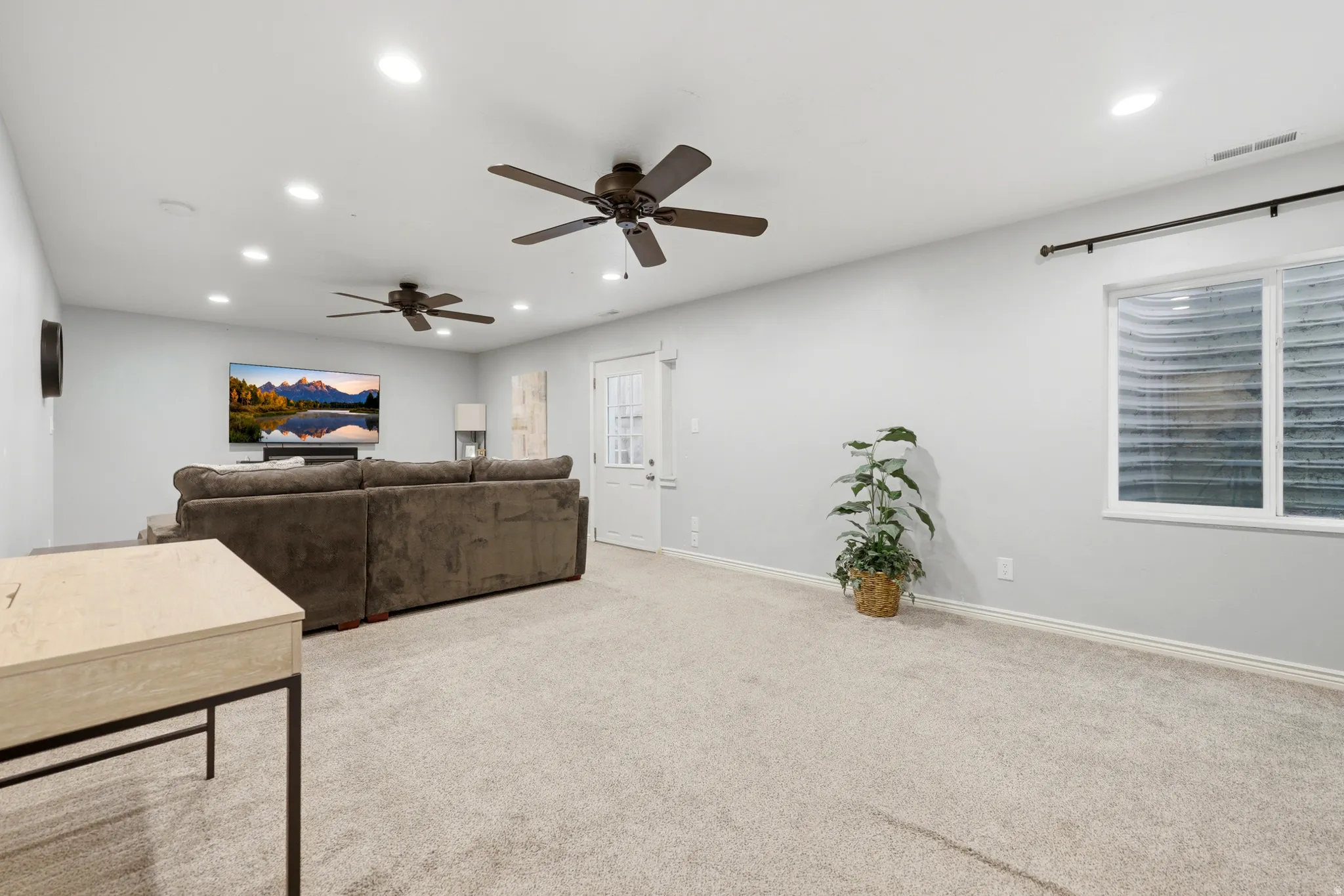 Spacious carpeted room featuring recessed lighting, two ceiling fans, a white paneled door, and a horizontal window with a window well