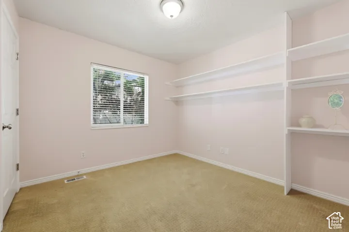 Carpeted room featuring a window with horizontal blinds, built-in shelving, white baseboards, and a flush mount ceiling light fixture