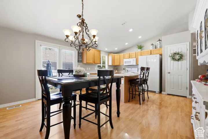 Open-concept dining and kitchen area featuring wood-finish flooring, a vaulted ceiling, and recessed lighting