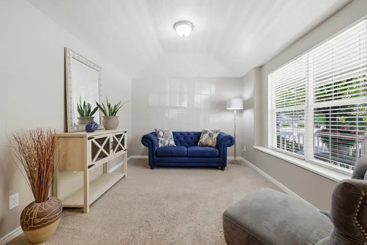 Vaulted ceiling room featuring light-toned carpeting, neutral wall paint, and multiple windows with horizontal blinds