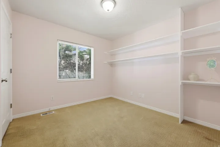 Carpeted room featuring a window with horizontal blinds, built-in shelving, white baseboards, and a flush mount ceiling light fixture