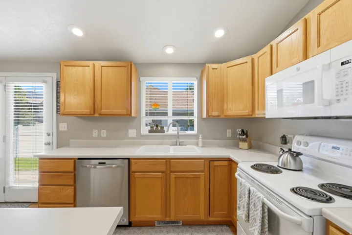 Kitchen featuring wood cabinetry, white countertops, stainless steel dishwasher, white range, and a dual basin sink