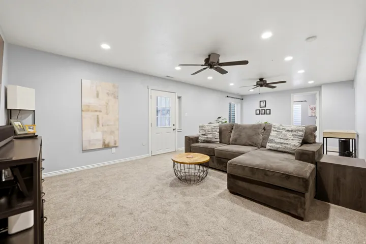 Expansive carpeted room featuring light gray walls, multiple recessed lights, two ceiling fans, and a white door with glass paneling