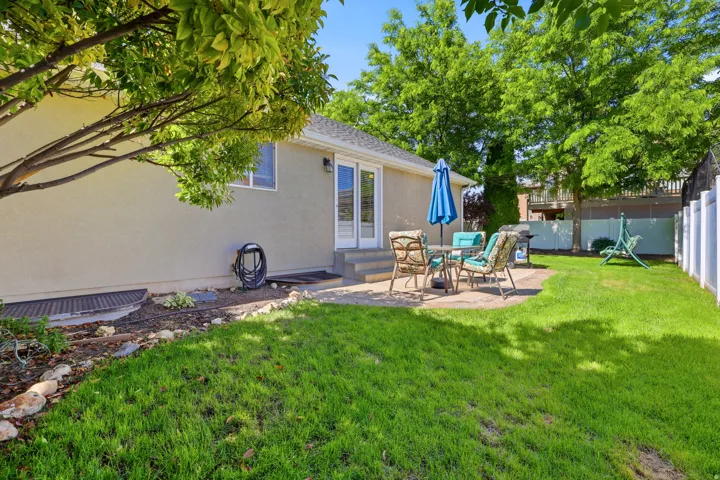 Expansive backyard featuring a manicured lawn, a paved patio area, and mature trees providing natural shade