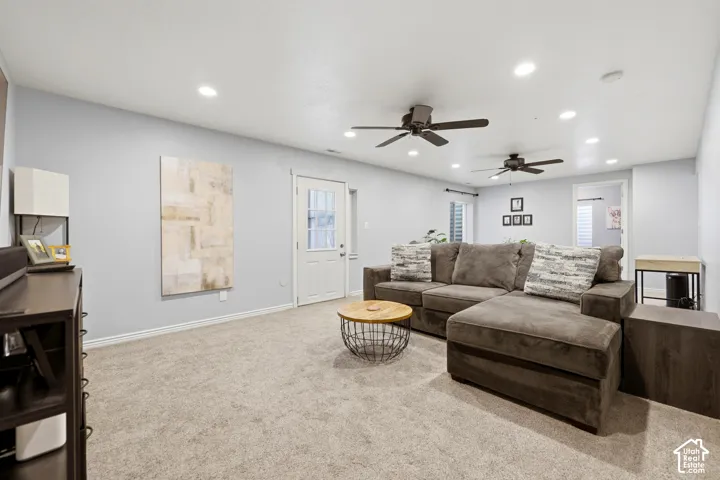 Expansive carpeted room featuring light gray walls, multiple recessed lights, two ceiling fans, and a white door with glass paneling