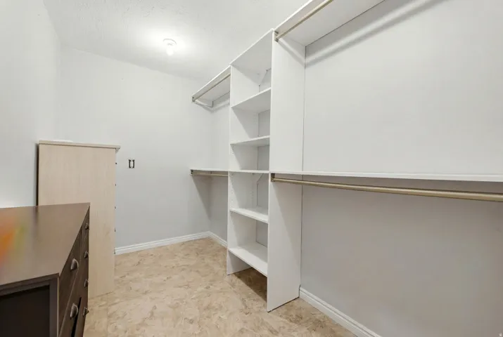 Spacious closet featuring white built-in shelving, hanging rods, and light-colored flooring