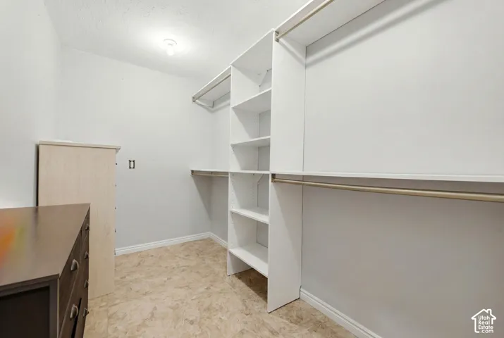 Spacious closet featuring white built-in shelving, hanging rods, and light-colored flooring