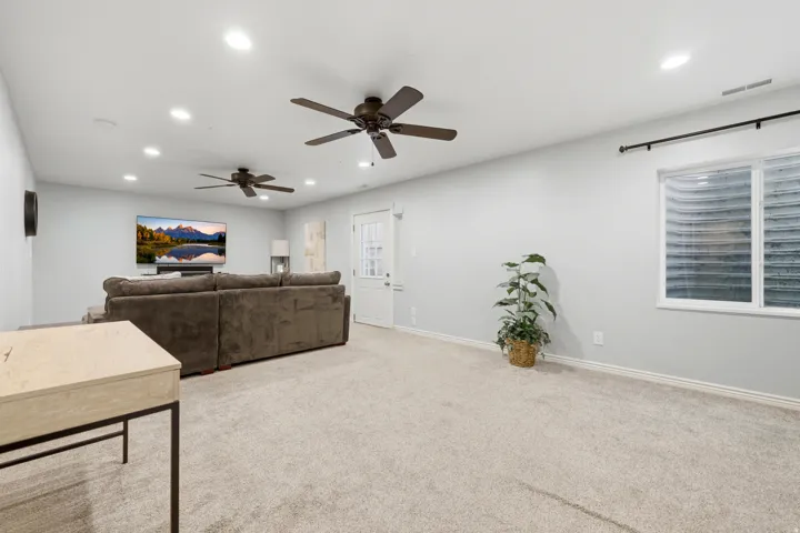Spacious carpeted room featuring recessed lighting, two ceiling fans, a white paneled door, and a horizontal window with a window well
