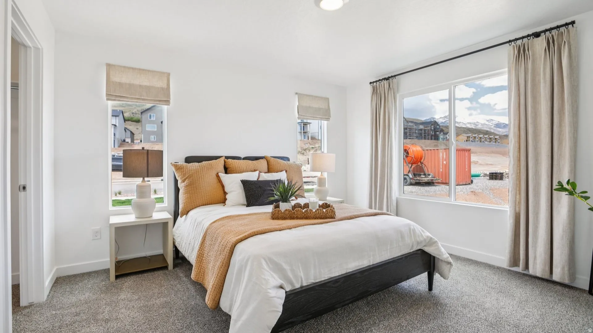 Bright bedroom with white walls, a large window, and gray carpeting