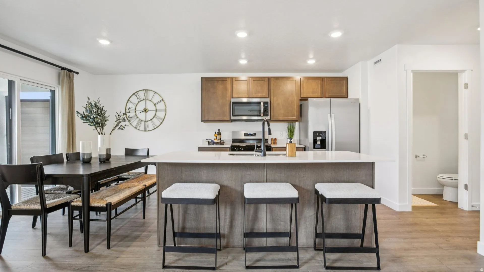 Open-concept kitchen featuring an island with a light-toned countertop, wood-finish cabinetry, and stainless steel appliances