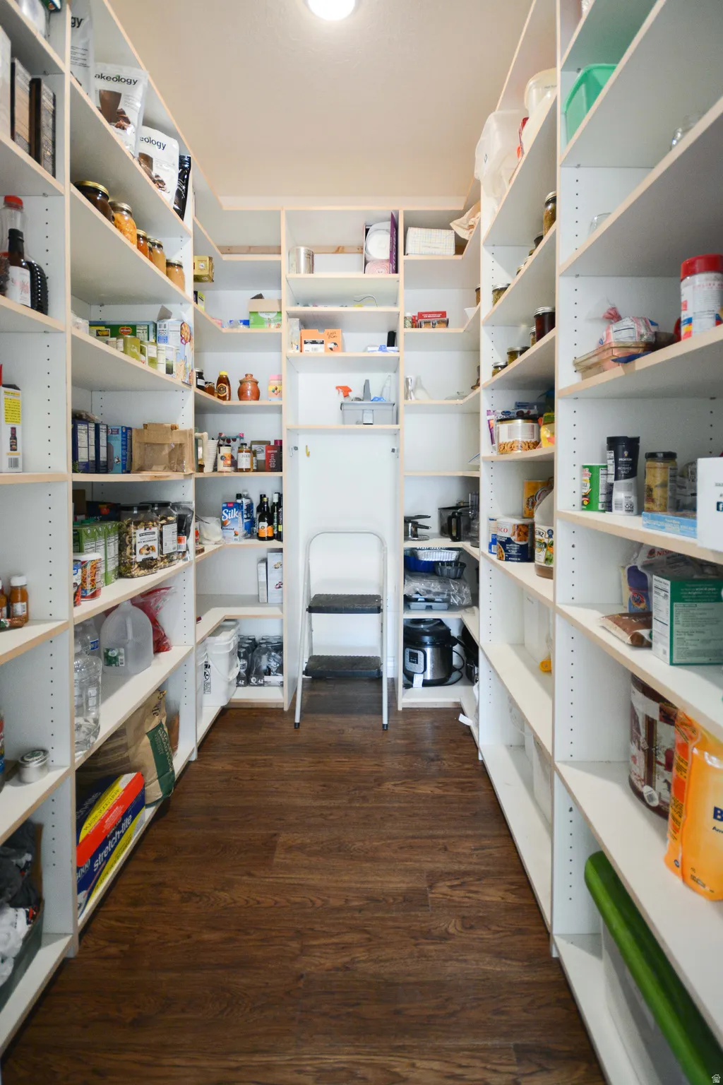 Spacious walk-in pantry featuring extensive white shelving, dark wood-finish flooring, and recessed ceiling lighting