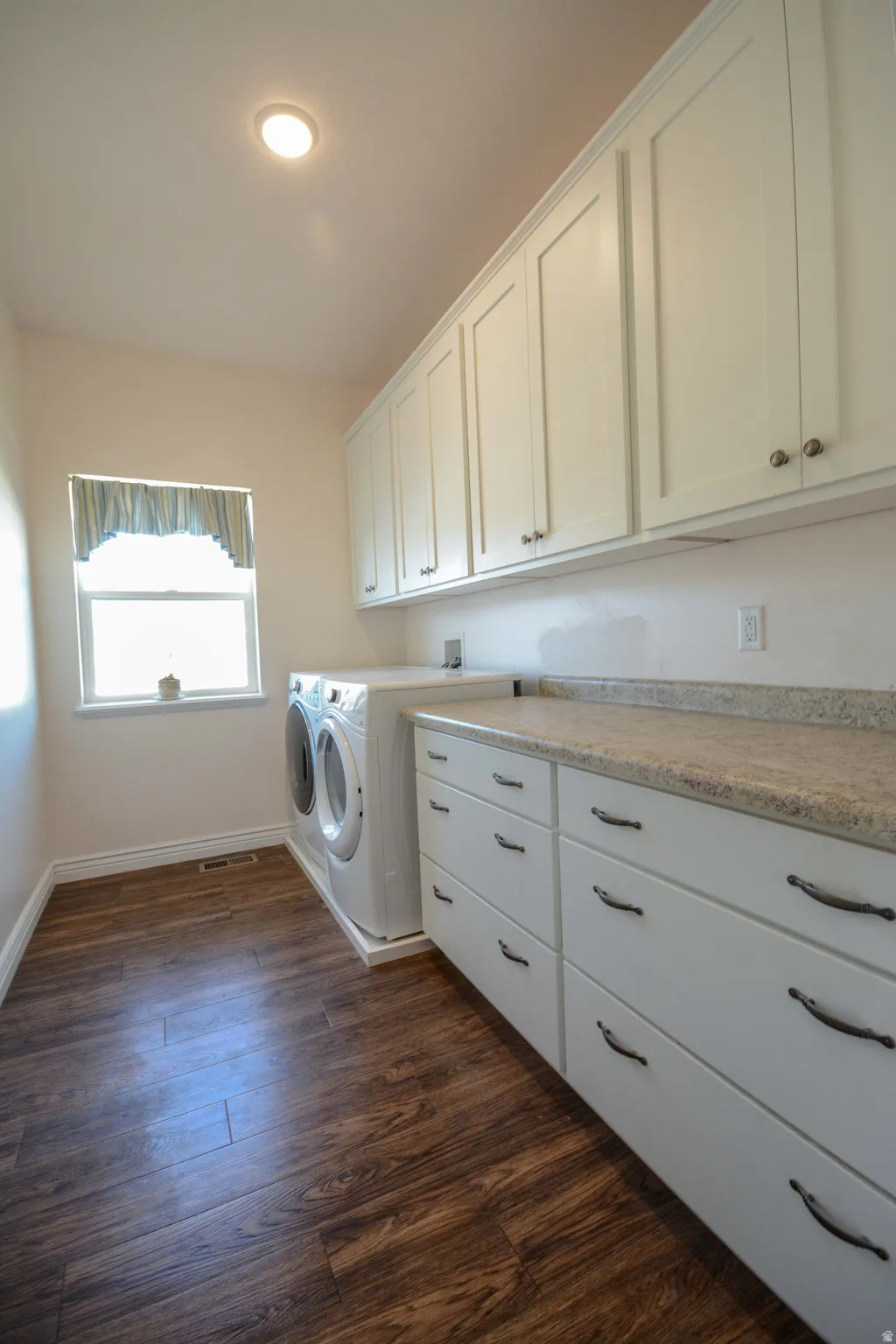 Laundry area featuring wood-finish flooring, white cabinetry, integrated counter space, and a window