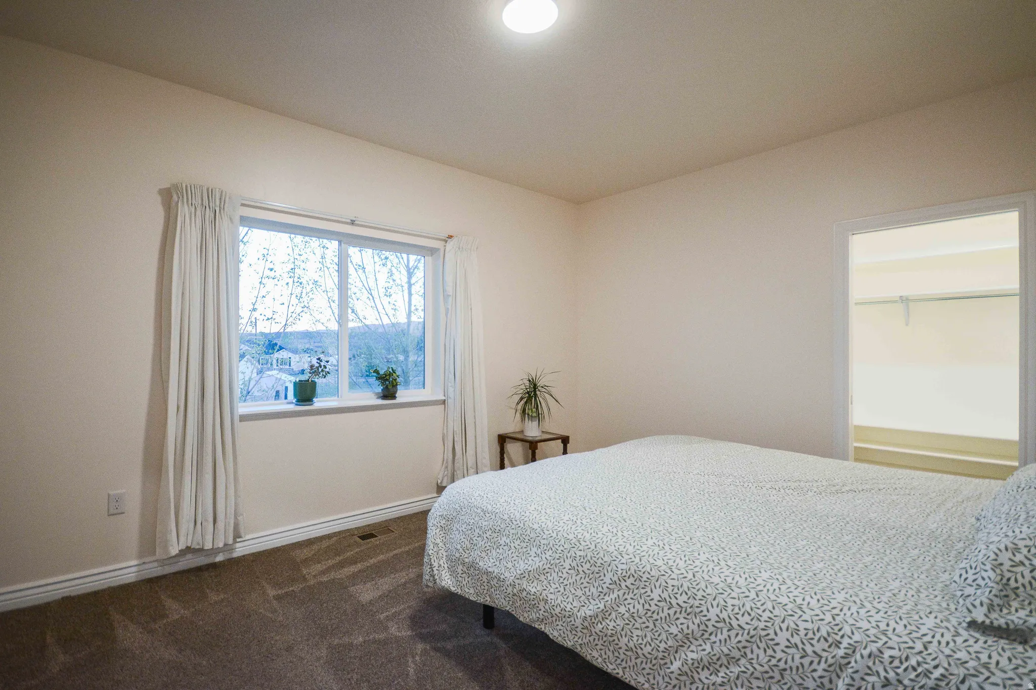 Spacious room featuring a large window, neutral wall paint, and brown patterned carpeting