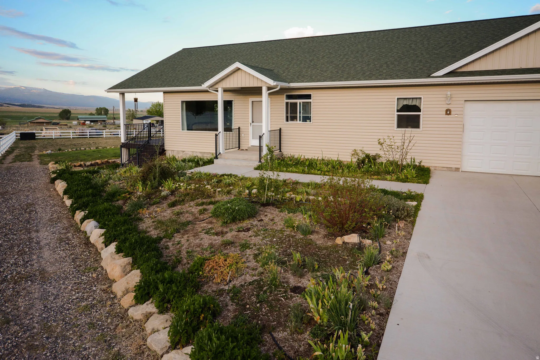 Beige siding exterior with a dark green shingle roof, featuring a covered front porch with white columns and black railings