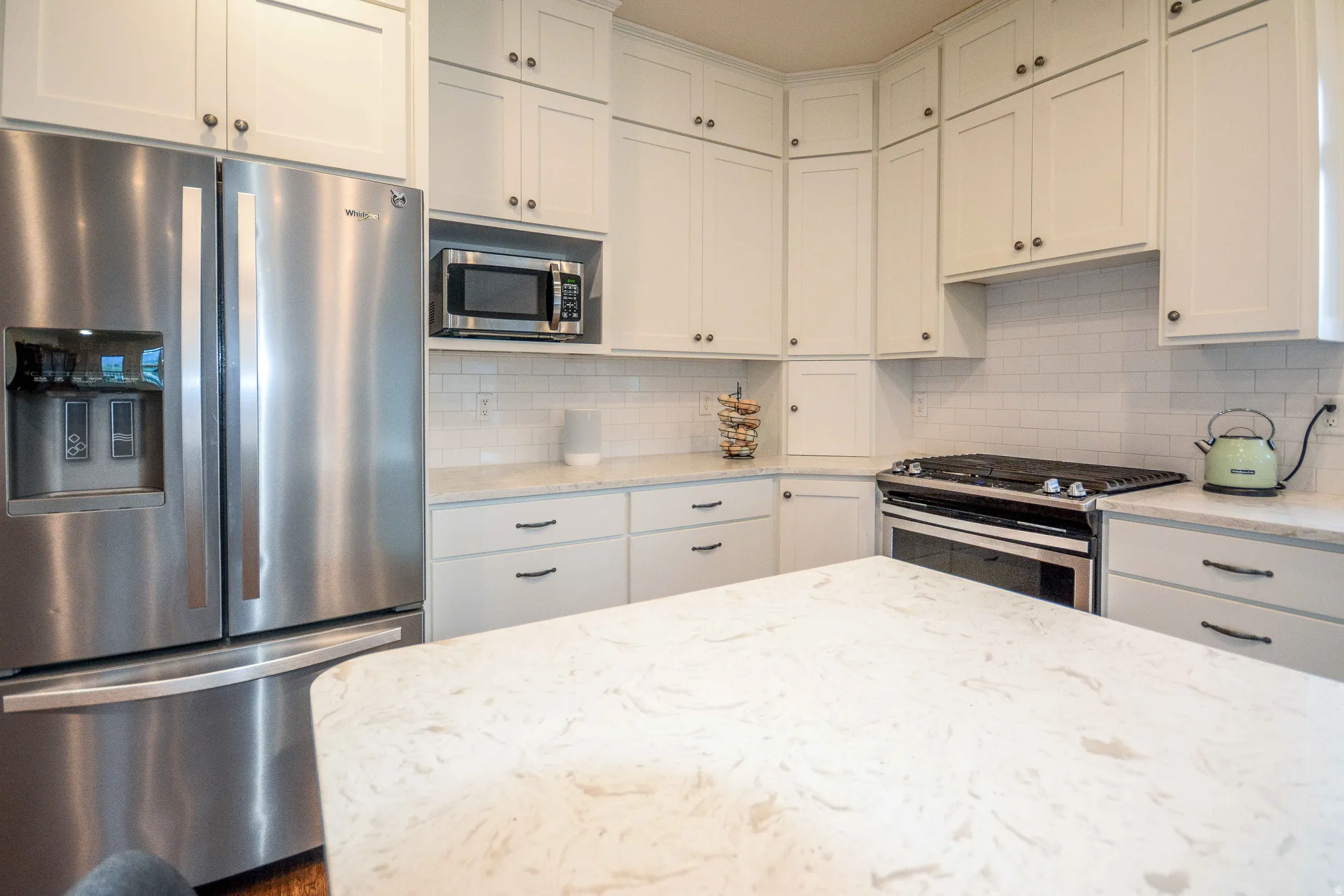 Kitchen featuring white shaker-style cabinetry, a built-in stainless steel microwave, a stainless steel gas range with oven, and a large central island with a light-toned countertop