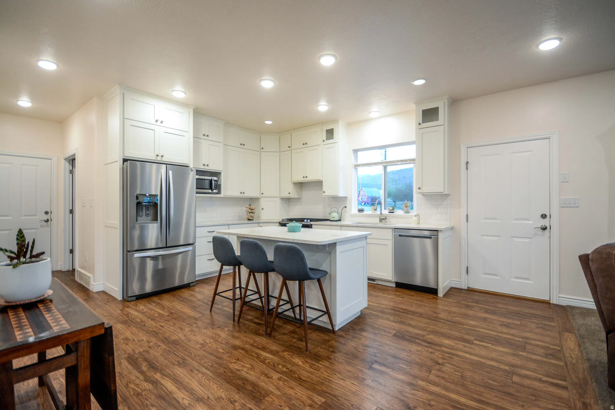 Kitchen featuring white cabinetry, stainless steel appliances, a center island with seating, a white subway tile backsplash, and wood-finish flooring