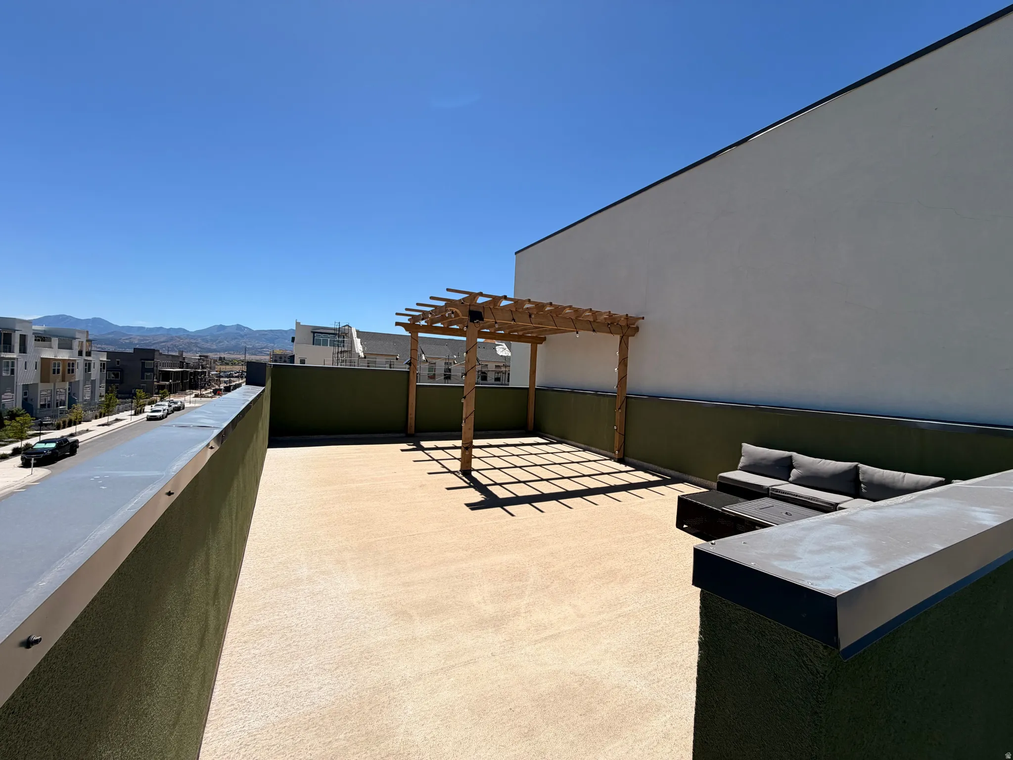 Rooftop patio featuring a wooden pergola, textured flooring, and a low green perimeter wall