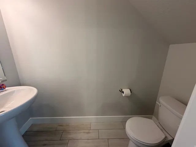 Bathroom featuring a white pedestal sink, a white toilet, and wood-finish tile flooring