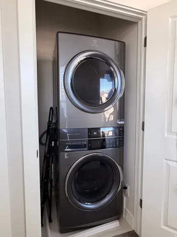 Dedicated laundry alcove featuring a stacked washer and dryer unit, front-loading design, control panel, and neutral wall tones