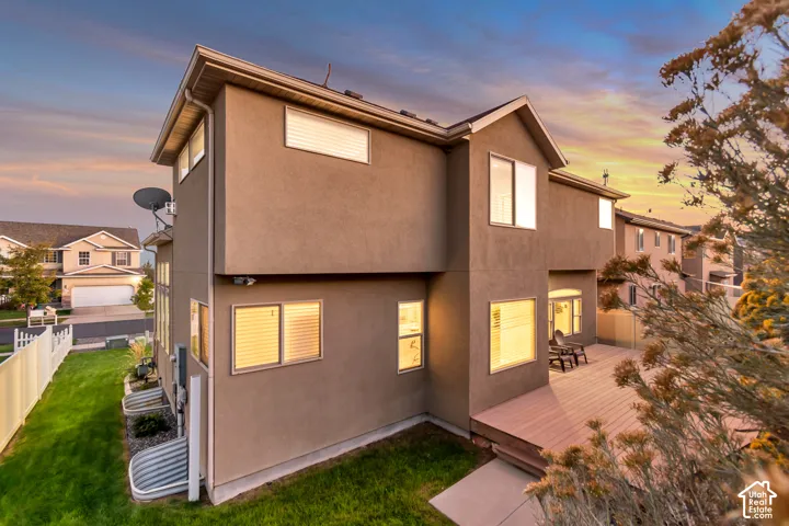 Multi-level stucco exterior with multiple windows, a composite deck, and a manicured lawn