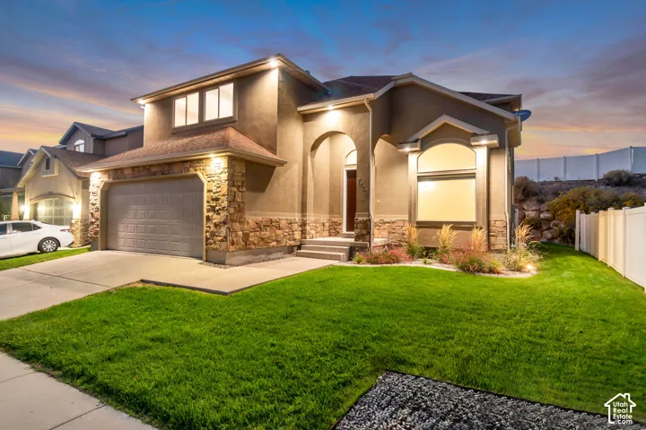 Stucco exterior with stone accents, attached two-car garage, front lawn, concrete driveway, and established landscaping