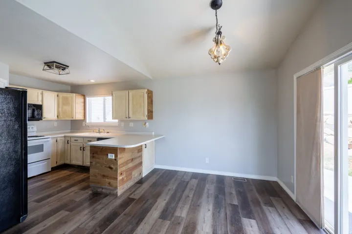 Open-concept kitchen and dining area featuring wood-finish flooring, light-toned cabinetry, light countertops, and a kitchen island with a wood-plank accent