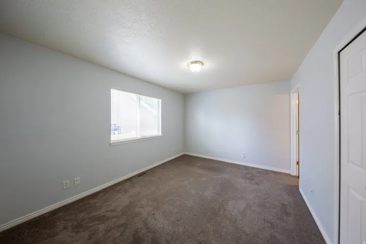 Carpeted interior space featuring light-toned walls, a single window, and a flush-mount ceiling light fixture