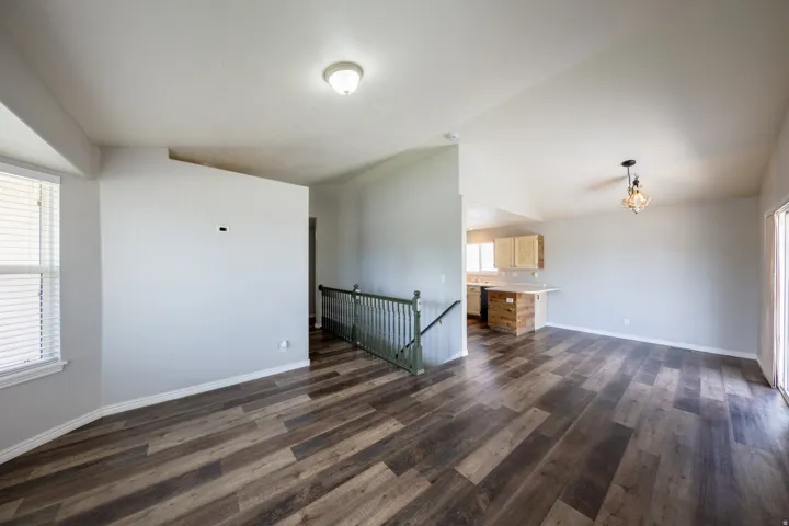 Spacious open-concept living area featuring wood-finish flooring, vaulted ceilings, and a decorative chandelier