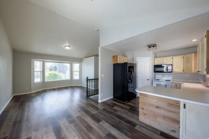 Open-concept living area featuring wood-finish flooring, a bay window, and vaulted ceilings