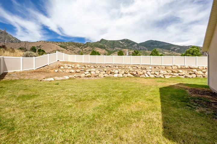 Expansive backyard featuring a manicured lawn, a rock retaining wall, and a tan privacy fence