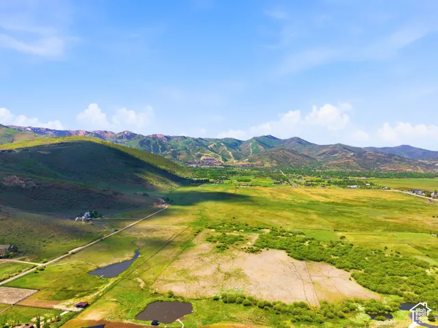 Expansive green landscape with distant mountains, two visible ponds, and scattered structures