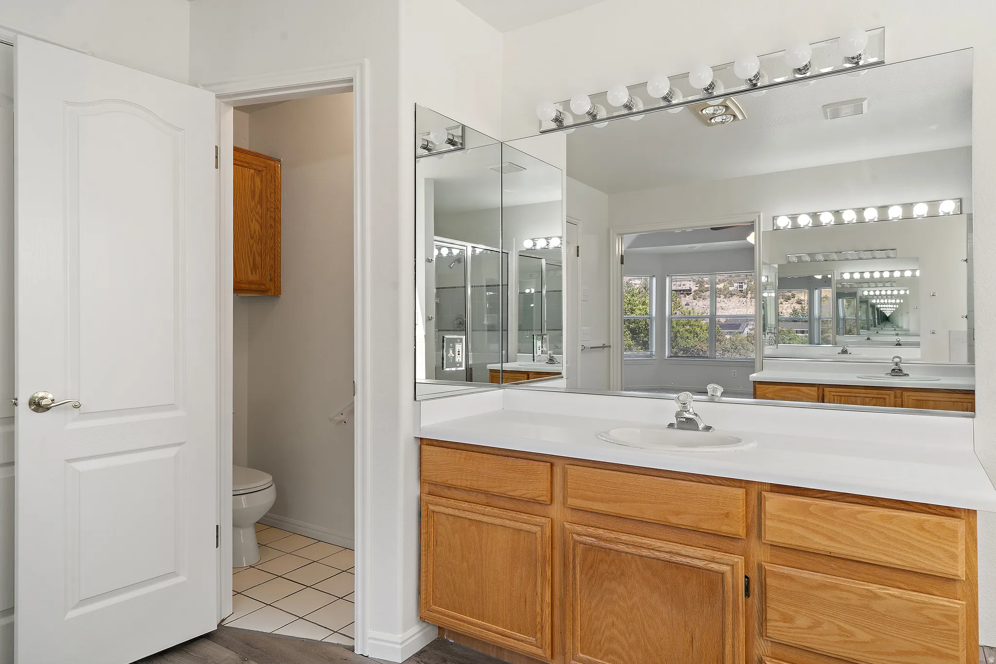 Bathroom vanity featuring a light-toned countertop with integrated sink, wood-finish cabinetry, and an expansive wall-mounted mirror