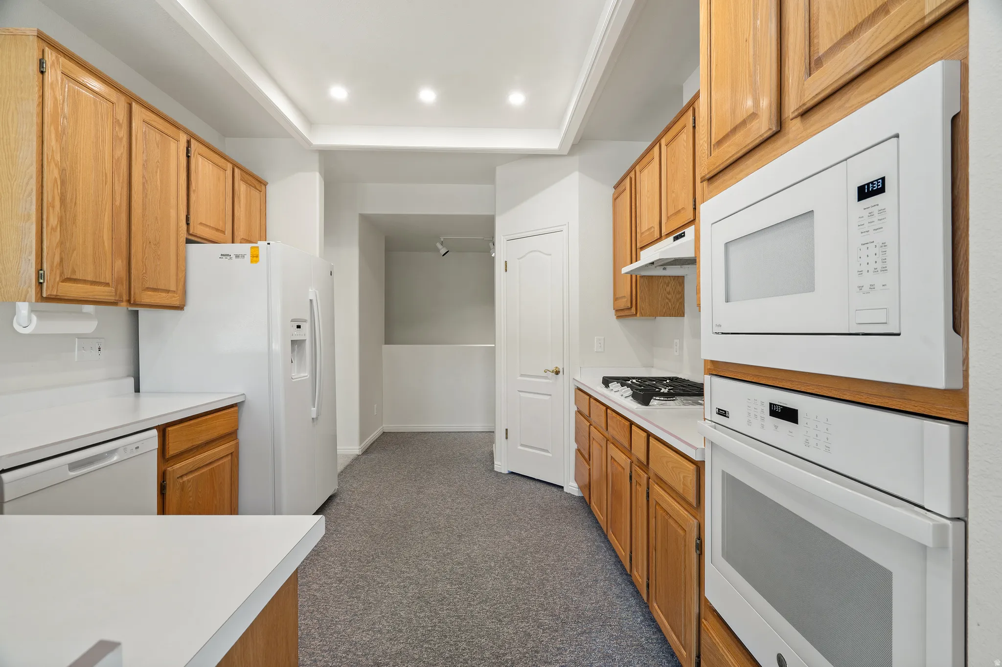 Kitchen featuring light wood cabinetry, white countertops, built-in white appliances, including an oven and microwave, and recessed lighting