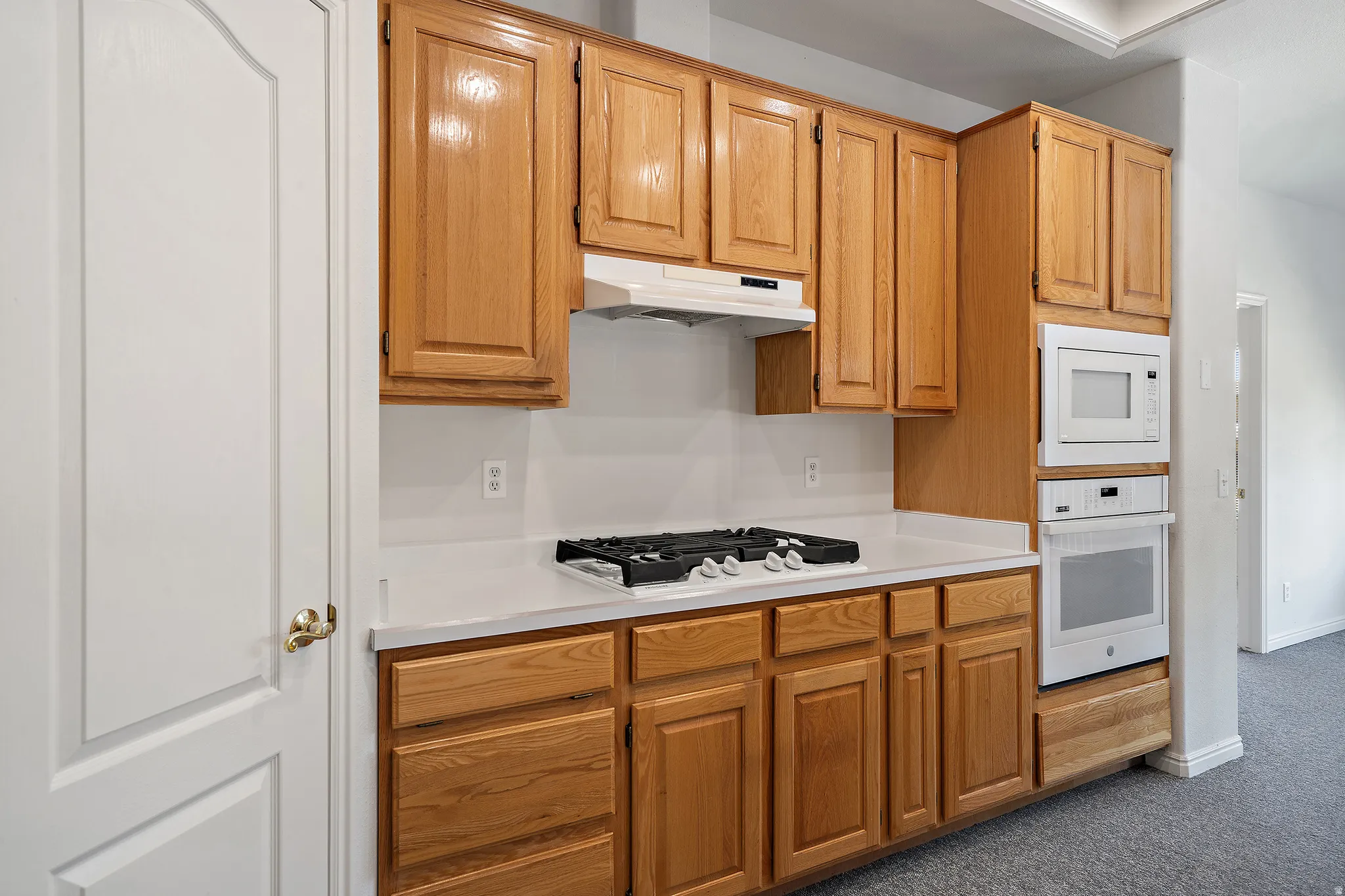 Kitchen featuring wood-finish cabinetry, white countertops, a built-in wall oven, a built-in microwave, and a gas cooktop with an overhead range hood